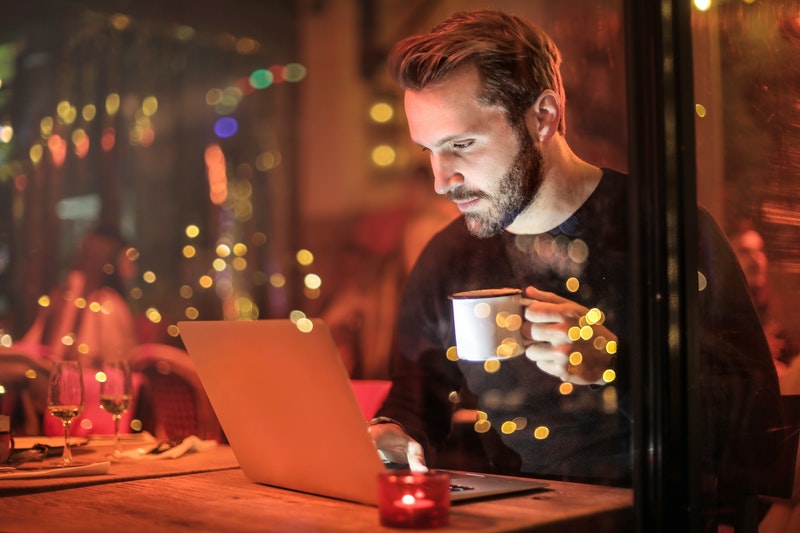A man holding tea of cup and watching to his laptop